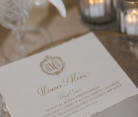Elegant dinner menu card with gold lettering, candles, glassware, and flowers at a Louisiana wedding; salad as first course.