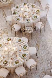 Overhead view of round reception tables styled with white florals, salads, gold flatware, and shimmering champagne linens.