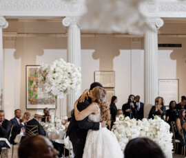 Bride and groom share their first dance in an elegant Louisiana wedding hall, surrounded by guests and white floral arrangements.