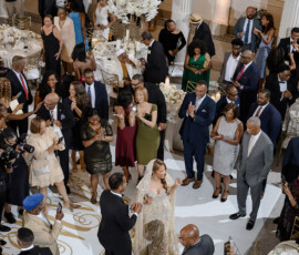 Bride and groom dance in an elegant room with guests watching, white flowers, and gold-accented tables for Gulf South wedding inspo.