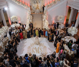 Woman in elegant gown on monogrammed floor at grand Louisiana-inspired wedding, surrounded by guests in formal attire.
