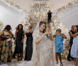 Bride in sparkling gown dances with guests on a flower-adorned staircase at vibrant New Orleans wedding reception.