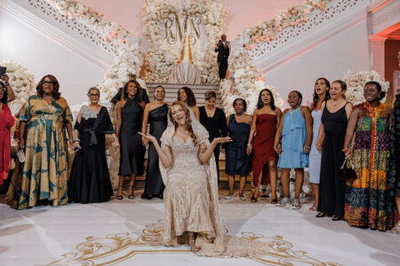 Bride seated at the center of the dance floor surrounded by guests holding hands during a lively wedding reception moment.