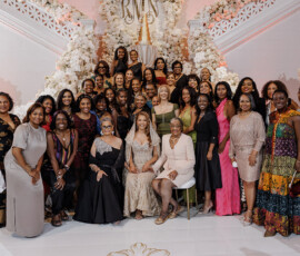 Women in formal attire pose at an elegant indoor event with white flowers and grand stairs, evoking Gulf South wedding style.