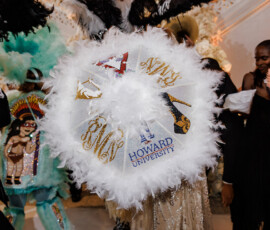 Person with a white Howard University umbrella amid colorful costumes at a lively, vibrant New Orleans wedding celebration.