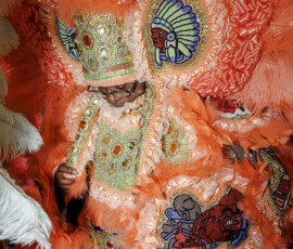 Person in an ornate orange feathered costume with Indigenous-inspired beadwork and decorated headdress, ideal for New Orleans weddings.