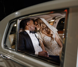 Bride and groom hold hands and share a kiss in the backseat of a classic car after their New Orleans wedding.