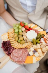 Charcuterie board with cheeses, crackers, fruits, and meats held by person in beige suit at elegant New Orleans wedding.