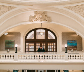 Couple stands on ornate balcony in grand building with arched ceilings, reflecting a timeless New Orleans wedding.