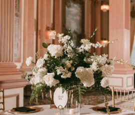 Banquet table with white floral centerpiece, black napkins, gold-edged plates, and candles in a grand Louisiana wedding venue.