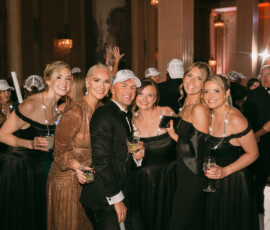 Six guests, dressed formally, smile and hold drinks at an elegant, warmly lit New Orleans wedding party.
