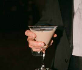 Elegant guest in formal wear with a pearl necklace holds a creamy beige martini at a New Orleans wedding.