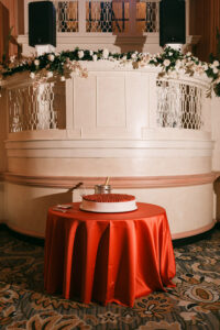 Strawberry-topped cake on a red tablecloth in front of a white, flower-decorated New Orleans balcony.