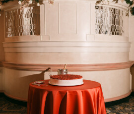 Strawberry-topped cake on a red tablecloth in front of a white, flower-decorated New Orleans balcony.