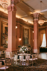 Luxurious ballroom with chandeliers, columns, gold chairs, round tables, and floral centerpieces for a Louisiana wedding.