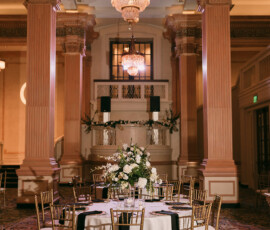 Banquet hall with tall columns, chandeliers, gold chairs, and a round table set for eight; elegant New Orleans wedding venue.