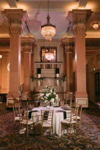Banquet hall with tall columns, chandeliers, gold chairs, and a round table set for eight; elegant New Orleans wedding venue.