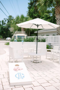 Outdoor patio with white chairs, table, umbrella, and cornhole game—ideal Louisiana wedding setting with palm trees and blue van.