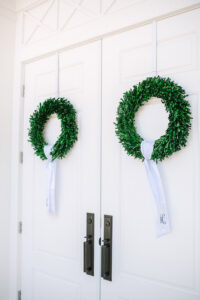 Green wreaths with white monogrammed ribbons adorn double white doors, evoking timeless, elegant New Orleans wedding style.