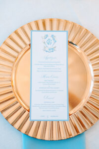 Elegant Gulf South wedding menu card with blue and gold accents for Cole and Morgan, displayed on a gold charger plate.