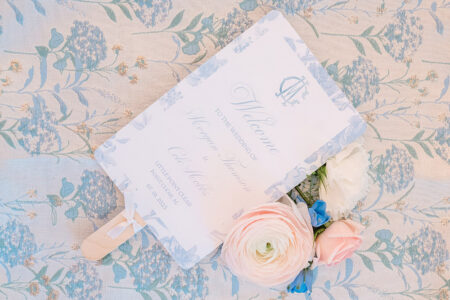Floral wedding program fan on patterned tablecloth with white, pink, and blue flowers at a Louisiana ceremony.