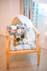 Bridal bouquet, white heels, blue ring box, gold perfume, and veil on wicker chair in romantic Louisiana wedding light.