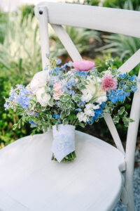 Pink, blue, and white flower bouquet with green leaves on a white wooden chair outdoors—ideal for a New Orleans wedding.