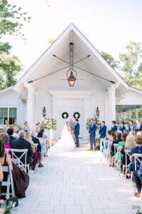Outdoor Gulf South wedding at a white chapel, with the couple at the entrance, guests seated, and formal wedding party.
