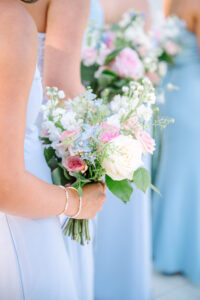 Bridesmaids in light blue dresses with white, pink, and blue rose bouquets at an elegant outdoor wedding ceremony.
