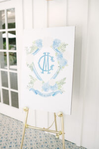 Elegant blue and white floral sign with CM monogram and July 19, 2025 date on gold easel, ideal for Louisiana weddings.