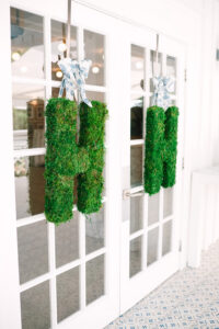 Green moss H letters hang from blue and white ribbons on glass doors in a bright, naturally lit room—ideal Gulf South wedding decor.