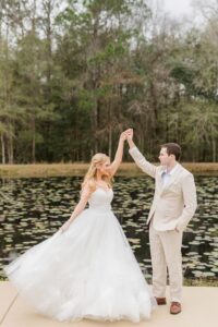 Bride in white gown twirls with groom by lily pad pond and trees, showcasing enchanting New Orleans wedding inspiration.
