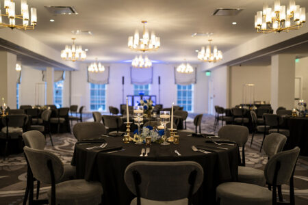 Chic Louisiana banquet hall with round tables, black linens, candles, and floral centerpieces under modern chandeliers.