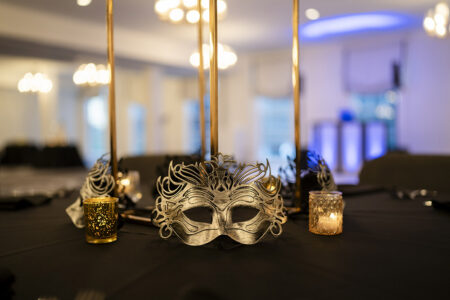 Silver masquerade masks and glowing candle votives decorate black linen reception tables with tall gold centerpieces at an elegant evening wedding reception.