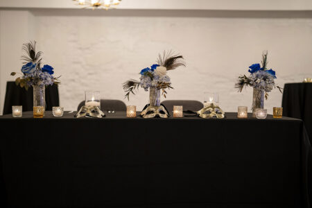 Black tablecloth table with blue and white flowers, candles, and metallic skulls at a Louisiana wedding reception.