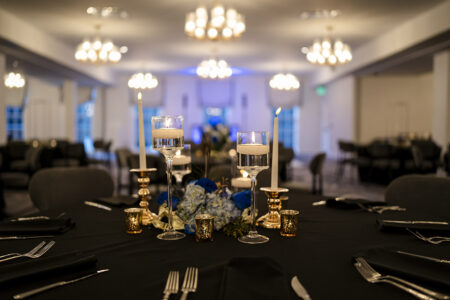 Banquet table with floating candles, gold holders, and blue florals in a softly lit Gulf South wedding hall.