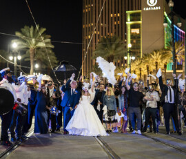 Newlyweds celebrate in the middle of a New Orleans street with guests, masquerade masks, and a brass band during a festive second line wedding parade.