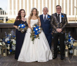 Newlyweds pose with family members during rooftop wedding portraits surrounded by blue and white floral ceremony arrangements and lantern accents.