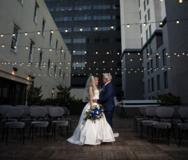 Bride and groom share a quiet moment alone on a rooftop wedding terrace framed by café lights and modern city buildings.
