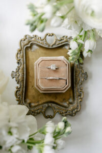 Engagement ring and wedding band in a velvet box on a brass tray with white flowers, capturing New Orleans wedding elegance.