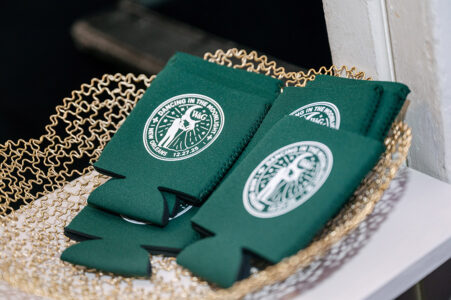 Green wedding koozies with a dancing couple logo displayed in a gold basket, ideal for New Orleans celebrations.