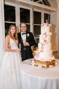 Bride and groom smiling by a four-tiered flower cake, holding champagne, at a classic New Orleans wedding.