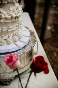 White ruffled wedding cake on silver stand with pearls, pink and red roses—ideal for an elegant Louisiana wedding.