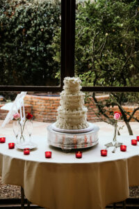 White tiered wedding cake with red candles and roses on a round table by a window at a New Orleans wedding reception.