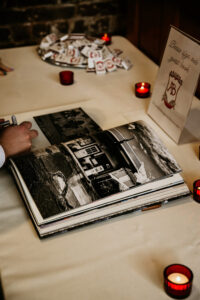 Guest signing a photo guestbook on a table with red candles, favor packets, and New Orleans-inspired black-and-white house photo.