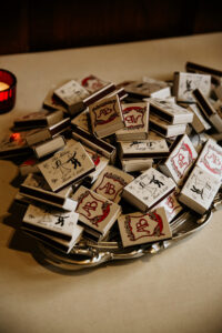 Custom AB wedding matchboxes on a silver tray beside a red candle—chic New Orleans wedding inspiration.