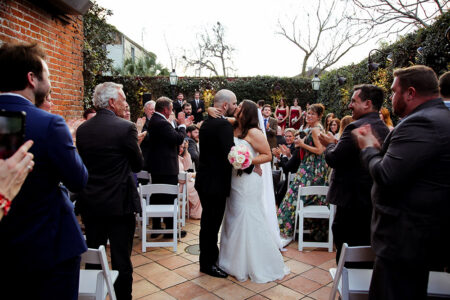 Bride and groom kiss at their Gulf South outdoor wedding, cheered on by guests lining both sides of the aisle.