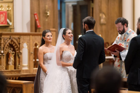 Bride and groom smile at the altar with a bridesmaid and officiant in a charming, wood-accented church wedding ceremony.