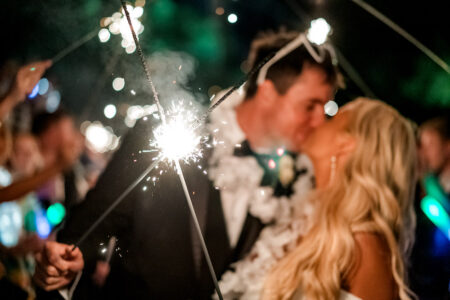 Bride and groom kiss at a New Orleans wedding, surrounded by sparklers; close-up sparkler in foreground, couple blurred.