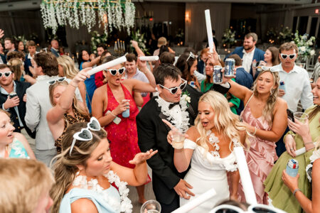 Guests in sunglasses and leis dance with the bride and groom indoors at a lively New Orleans wedding celebration.